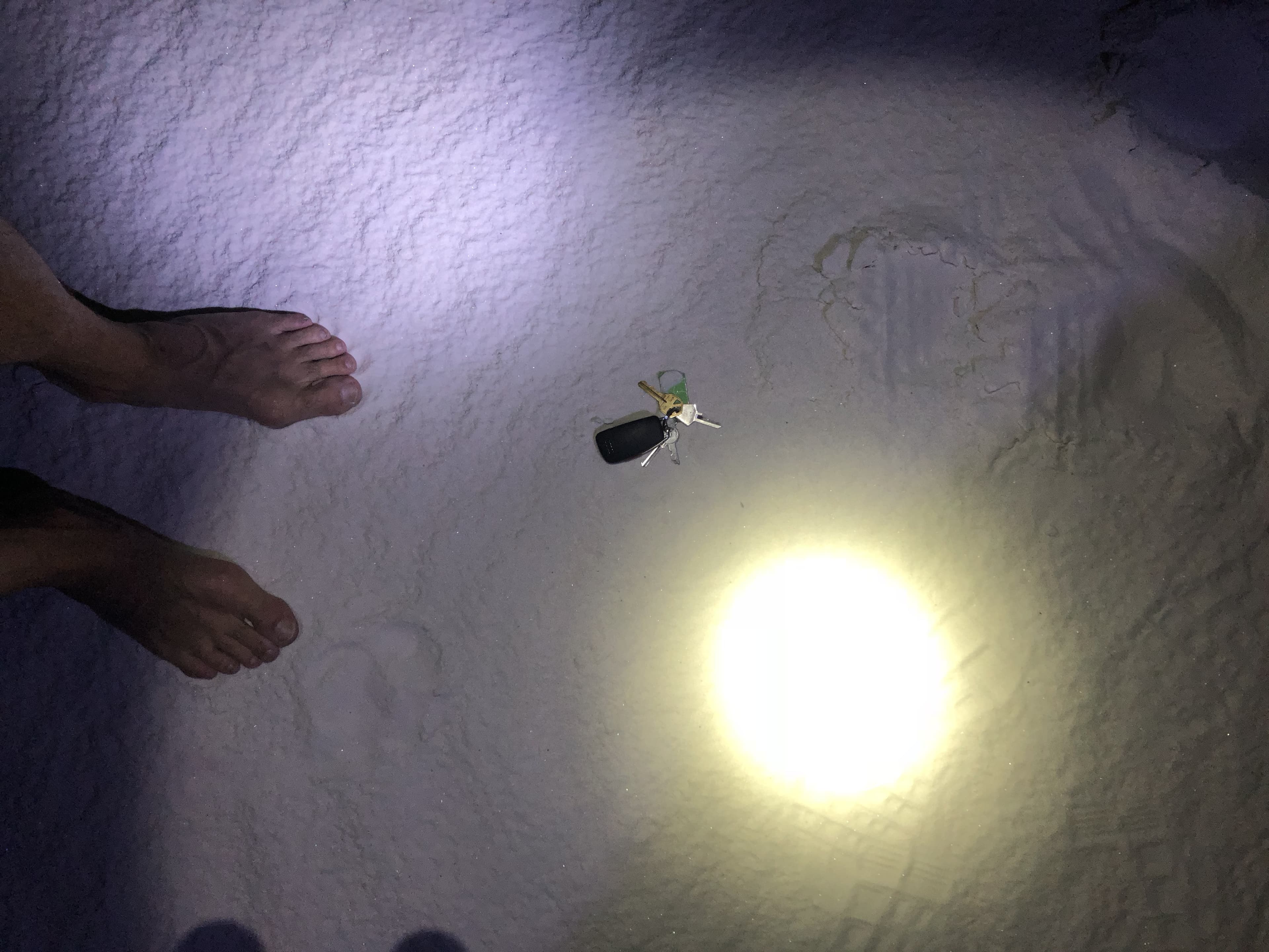 The lost car keys lying in the sand under a flashlight beam